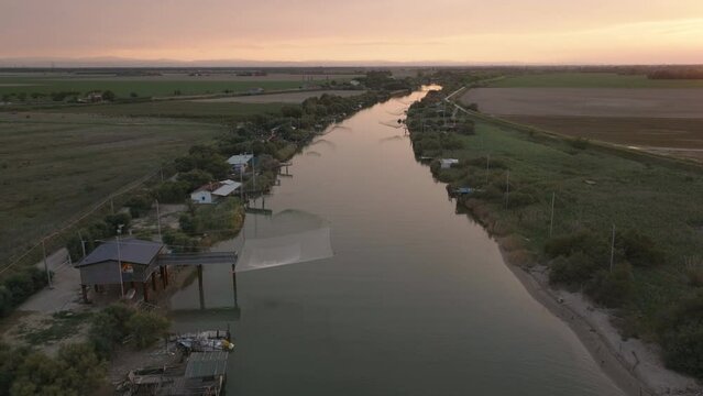 Aerial view 30 fps of fishing huts on shores of estuary at sunset