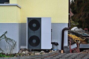 Dark grey colour air source heat pump installed outside the house painted grey and pastel yellow...