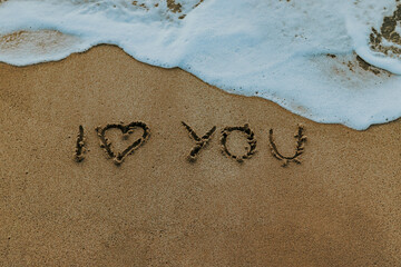 Horizontal high angle shot with love message on the beach sand.