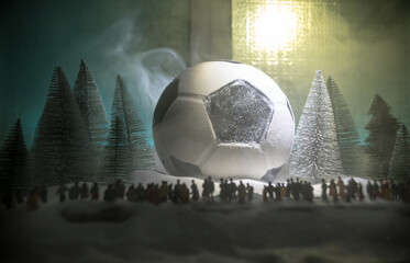 World cup at wintertime concept. Football (Soccer) ball on snowy decorated table with toy miniatures. New Year Christmas theme. Selective focus.