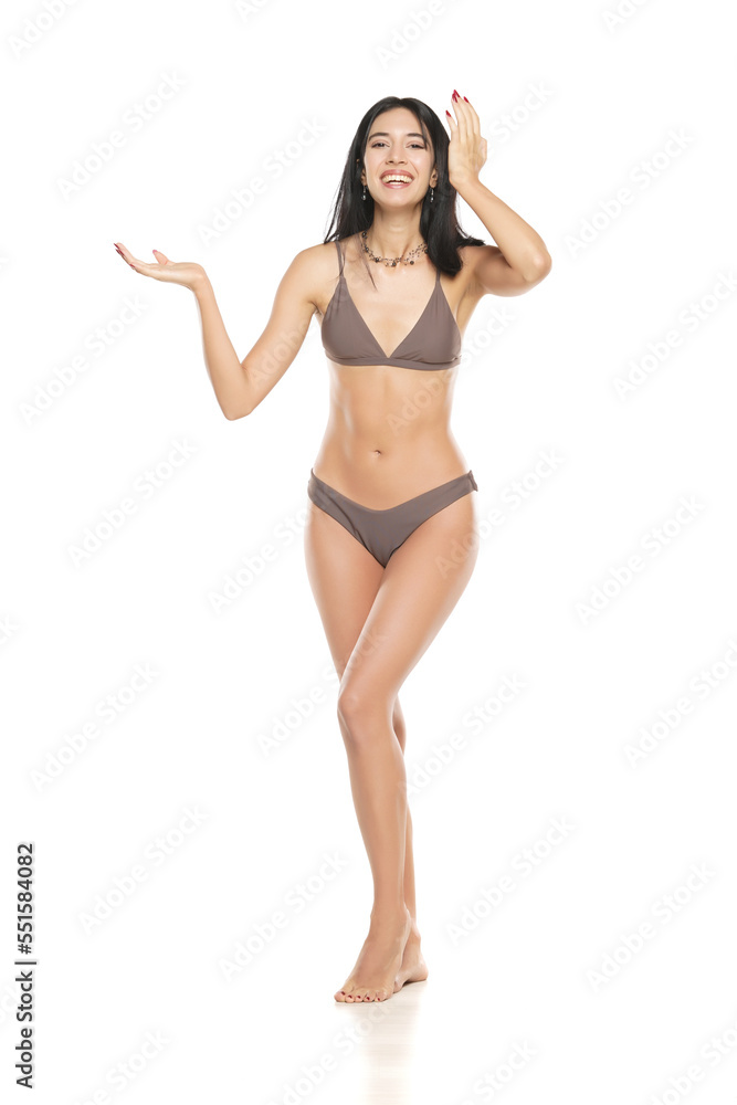 Wall mural young smiling brunette woman in bikini swimsuit advertising imaginary object on her hand on a white 