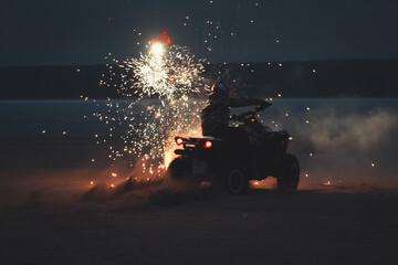 Athlete on a quad bike rides at night on a sandy beach with fireworks © Елена Вырыпаева