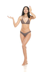 Fototapeta premium Young smiling brunette woman in bikini swimsuit advertising imaginary object on her hand on a white background.