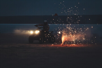 Athlete on a quad bike rides at night on a sandy beach with fireworks © Елена Вырыпаева