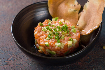 salmon Tartar with avocado on black plate on dark stone table macro close up