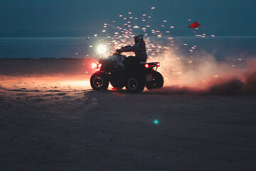 Athlete on a quad bike rides at night on a sandy beach with fireworks © Елена Вырыпаева