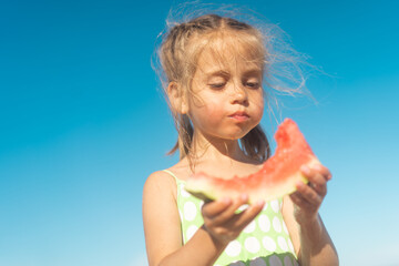 Funny little girl eat watermelon sunny summer day at ocean beach. Cute caucasian female child enjoy summer fruit bite slice of watermelon. Happy childhood.