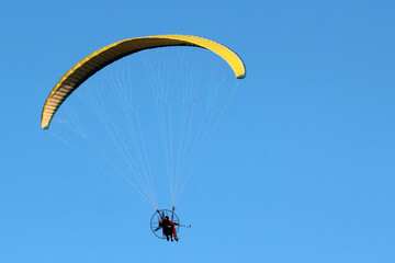 Paragliding in a blue sky, pilot controls motorized flying machine