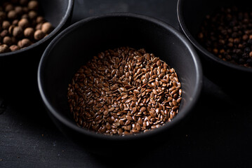 Linseed in black bowl. Dark background. Closeup view.