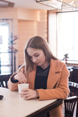beautiful young woman with a glass of takeaway coffee sits in a cafe stir sugar in coffee