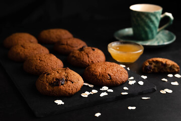Blurred image of oatmeal cookies, honey and a cup of tea on a dark table.
