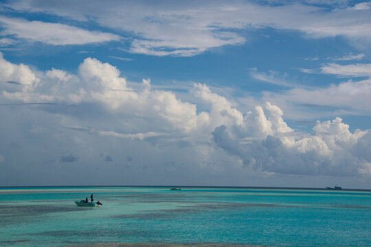 A boat at the surface of a coral reef in the Maldives with large clouds in the sky