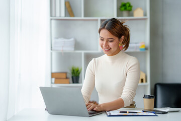 Beautiful young Asian businesswoman sitting working with laptop thinking about new ideas for her work with a bright and happy face.