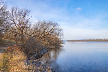 View along shore of a wide calm river in early winter, daytime, nobody