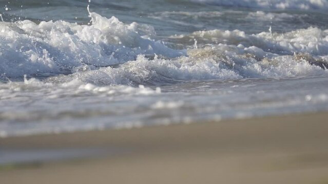 Closeup of waves splashing wet beach sand drying, cinematic dof
