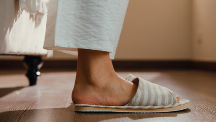 Close-up Asian girl foot step down on bed with white pajamas wear slipper walk to open curtain on window fresh peaceful morning light empty floor in bedroom at home. Female morning lifestyle concept. - obrazy, fototapety, plakaty