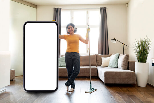 Young Arab Woman Cleaning Home And Standing Near Big Blank Smartphone