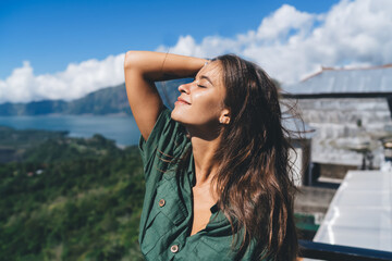 Positive woman touching hair in mountains
