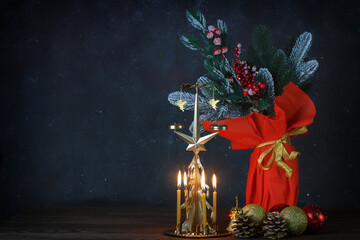 Golden Christmas tree-carousel candlestick with burning candles and a vase with a bouquet of fir branches on a dark vintage background among the Christmas decor
