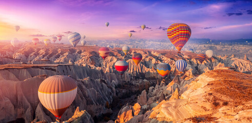 Aerial view amazing sunrise landscape in Cappadocia with colorful hot air balloon fly in sky over deep canyons, valleys. Concept banner travel Turkey - obrazy, fototapety, plakaty