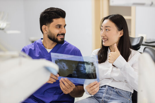 Medicine, dentistry and oral care concept. Male confident dentist showing x ray picture to attractive young patient, asian woman at modern light dental clinic.