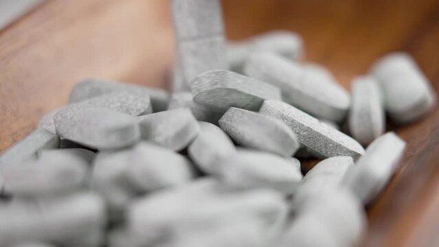 Tryptophan sedative pills falling on a wooden rustic surface in slow motion. Medical remedy for depression and insomnia. Natural pharmaceutical antidepressant