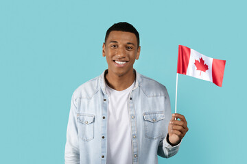 Happy young african american male student in casual show Canada flag, isolated on blue background, studio