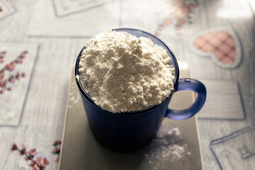 A full glass of flour. A blue glass filled with flour is on the table