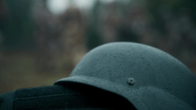 Soldier's PASGT kevlar combat helmet under raindrops with soldiers in the background on a battlefield