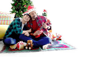 Adorable young LGBT couple sharing special moment together on Christmas holiday, Asian gay male lover singing song while playing ukulele in living room Merry Christmas happy winter holiday celebration