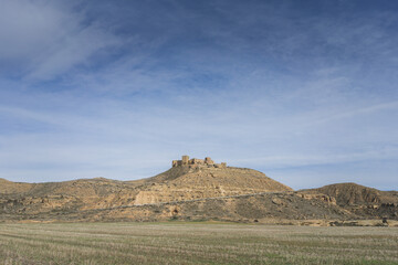 Dry landscape with a mountain on the horizon and at the top is the medieval castle of Montearagón with many ruins inside. Huesca, Spain