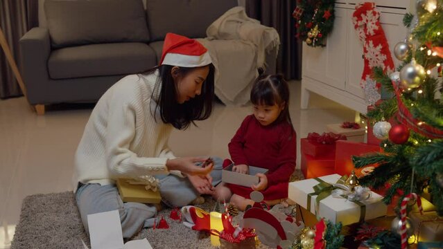 Asian young happy family enjoy New year holidays party together in house at night. Mom and kid present gift box together near Christmas tree decoration. Lifestyle celebrate holiday vacation concept.
