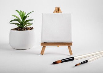 Square canvas on wood mini easel, blank mock up on wood tripod, paintbrushes and potted plant...