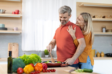 Happy grateful woman hugging her husband from behind, kitchen interior