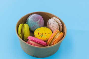 Colorful macaroons or macaron in a cardboard box on light blue background close up.