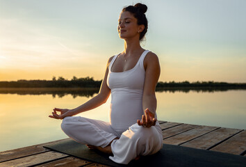 Fototapeta na wymiar Pregnant woman doing yoga at lake during sunset.
