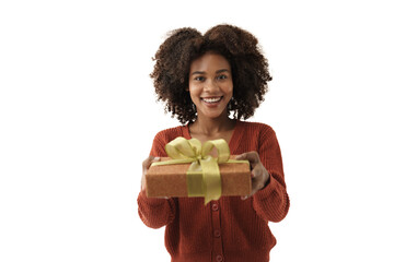 Cute African American young woman in knitted sweater gives a gift box to the camera on white wall...