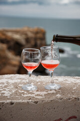Two wine glasses on the background of the sea and mountains. Pink champagne. The drink is poured from the bottle into glasses.