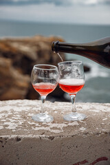 Two wine glasses on the background of the sea and mountains. Pink champagne. The drink is poured from the bottle into glasses.