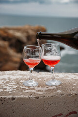 Two wine glasses on the background of the sea and mountains. Pink champagne. The drink is poured from the bottle into glasses.