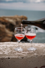 Two wine glasses on the background of the sea and mountains. Pink champagne. The drink is poured from the bottle into glasses.