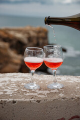 Two wine glasses on the background of the sea and mountains. Pink champagne. The drink is poured from the bottle into glasses.