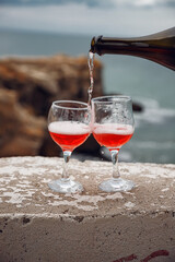 Two wine glasses on the background of the sea and mountains. Pink champagne. The drink is poured from the bottle into glasses.