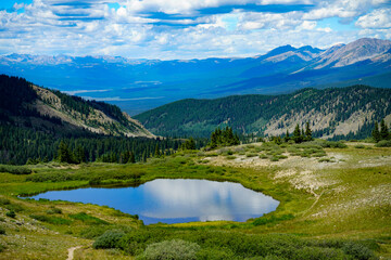 Naklejka na ściany i meble An alpine lake atop a Colorado mountain pass reflects the colors of a clouded blue sky.