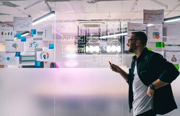 Focused man looking at data on glass wall in meeting room in office
