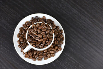 Coffee beans in white cup on dark wooden table, top view. Dark and roasted coffee, concept of natural drink