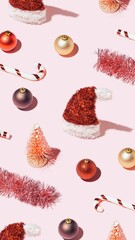 Trendy vertical Christmas wallpaper with red New Year's decorations on pastel pink background. Xmas pattern made of shiny props.