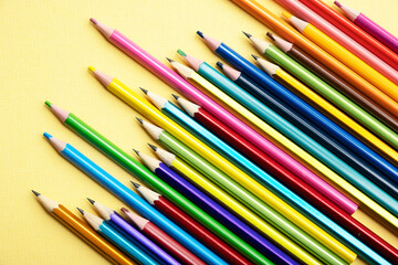 There are many different colored pencils scattered on a colored background.