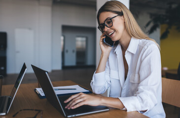 Cheerful woman with laptop talking on smartphone