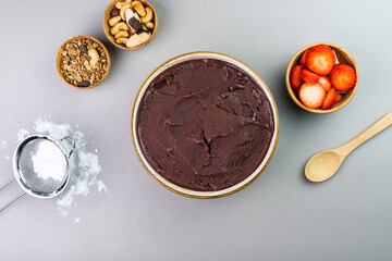 Brazilian açai in a white bowl, additional strawberry, granola and nuts in small bamboo bowls. Cashew nuts and Pará. Top view. Grey background. Selective focus